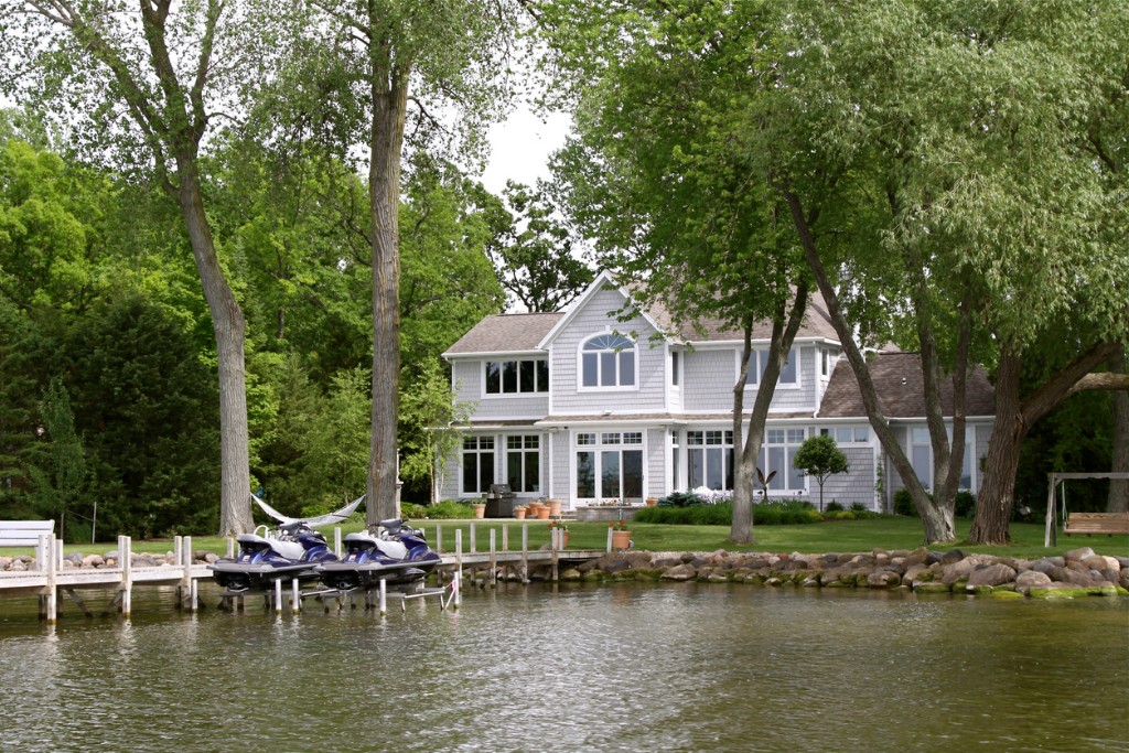 white house with brown tiled roof by the lake with jet ski's parked in front